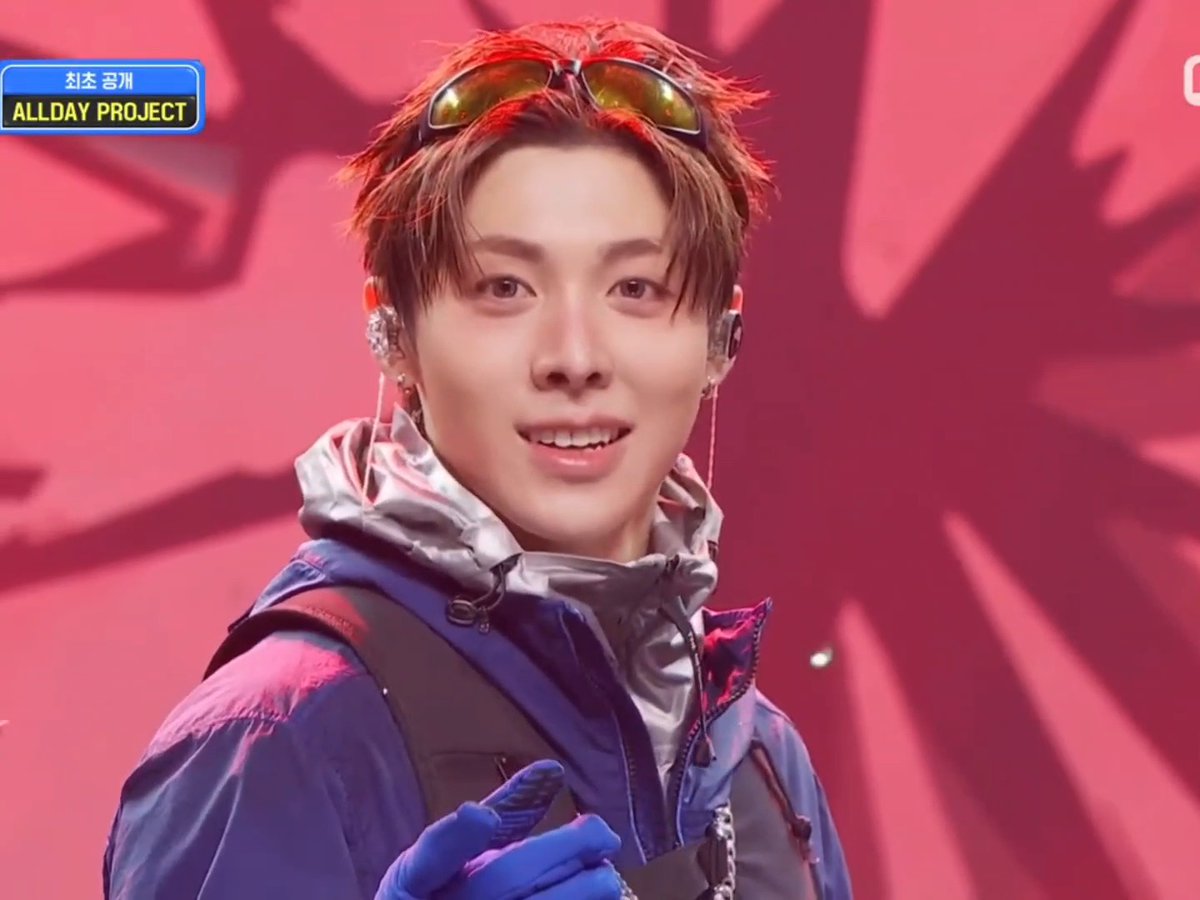A K-pop performer from 'ALLDAY PROJECT' with the name '최초 공개' (first reveal) in the corner, wearing sunglasses on his head and a silver and purple jacket.