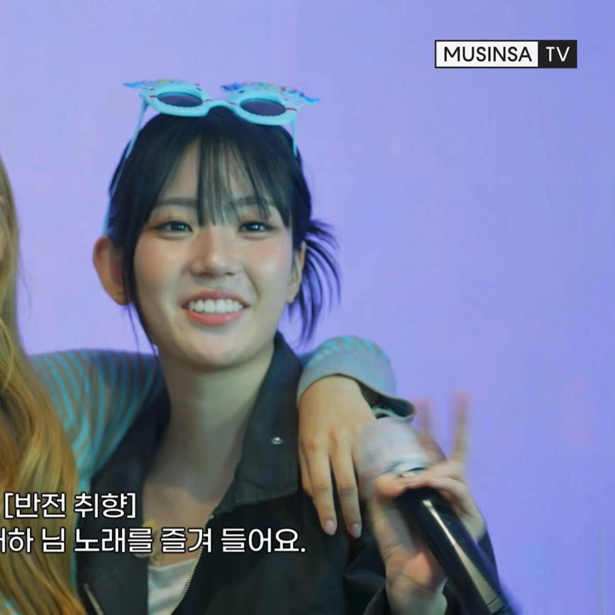 A young woman with dark hair and light blue sunglasses on her head smiles while holding a microphone, with 'MUSINSA TV' in the top right corner and Korean text '[반전 취향] 하 남 노래를 줄게 들어요' at the bottom.