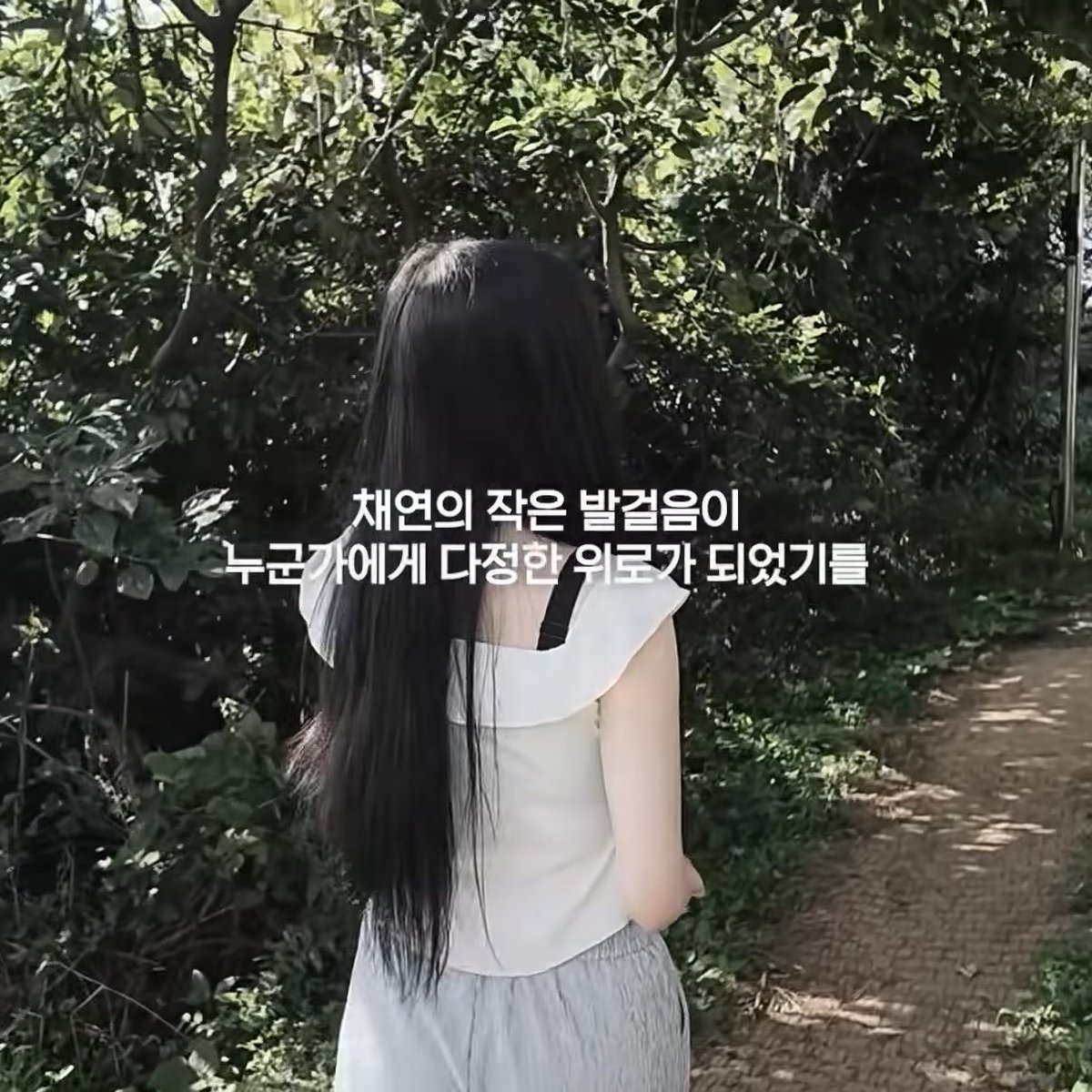 A person with long black hair viewed from behind, wearing a white top, walking along a forest path with Korean text overlay about giving diverse medicine to the young.