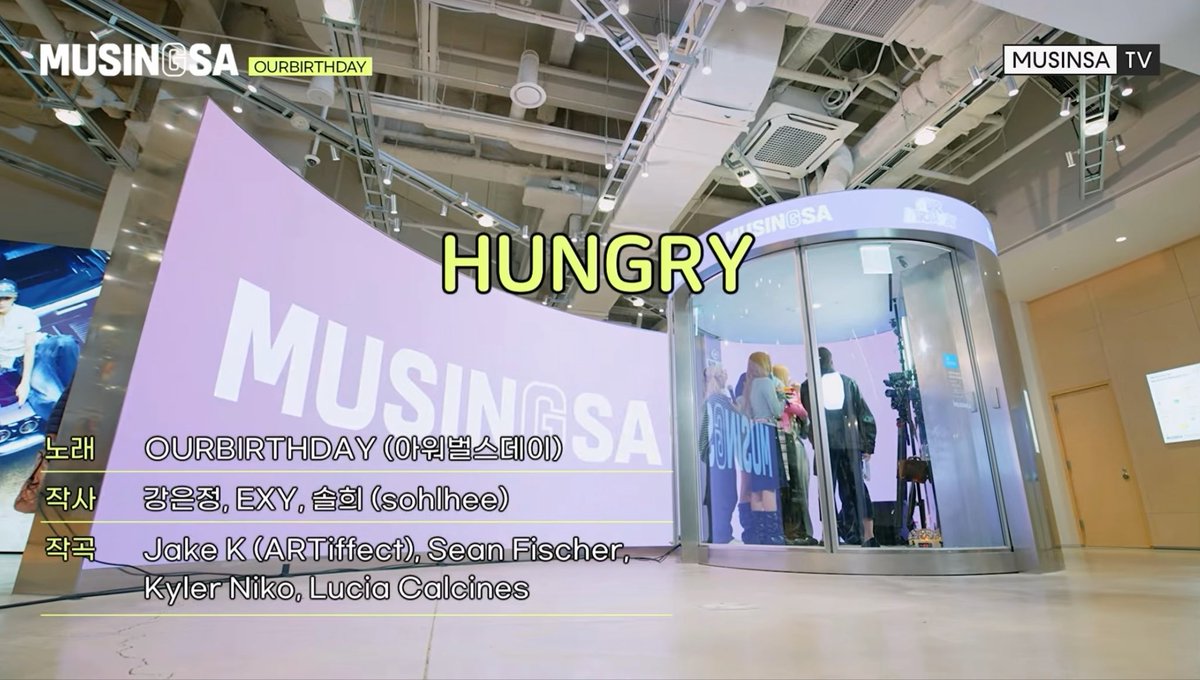 A still from 'MUSINSA TV' showing an event space featuring a large curved display reading 'HUNGRY MUSINSA' and credits for the song 'OURBIRTHDAY'.