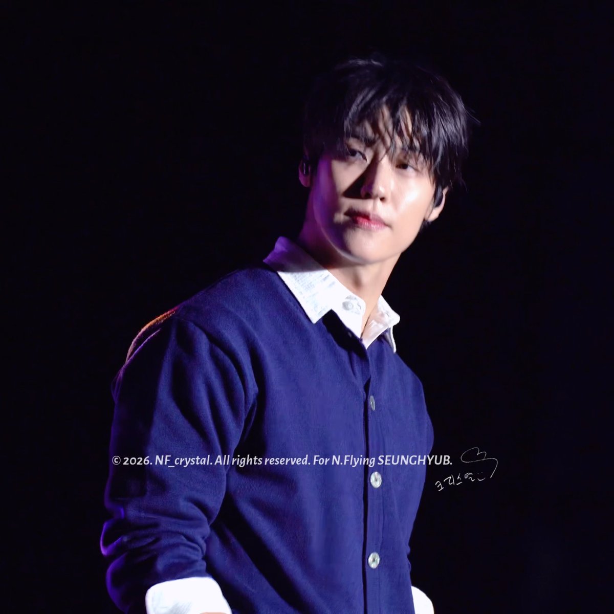 The image shows Lee Seung-hyub of N.Flying performing at the Seo-il University Festival (261001), wearing a navy blue cardigan over a white collared shirt. The watermark reads "© 2026. NF_crystal. All rights reserved. For N.Flying SEUNGHYUB" with a signature, matching the post's reference to the Bluemoon university festival performance.