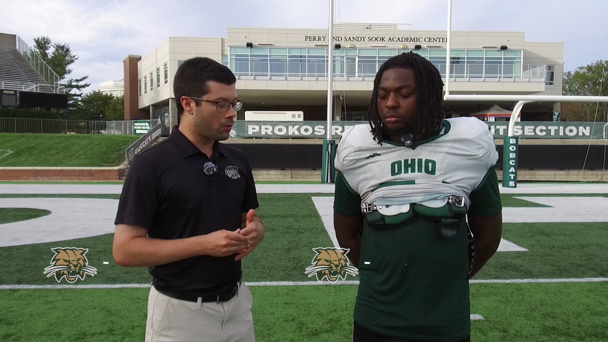 A reporter interviews Ohio University running back Irving Brown on the football field outside the Perry and Sandy Sook Academic Centre and Peden Stadium, capturing his thoughts on the running back room's strong bond and shared mindset that drives the team's success.