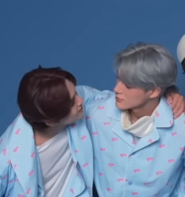 Two young men in matching light blue pajamas with a pink pattern embracing against a blue background.