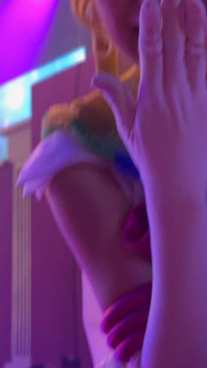 A blurry, purple-toned selfie showing a person with their hand near their face, holding what appears to be a plush toy or costume accessory.