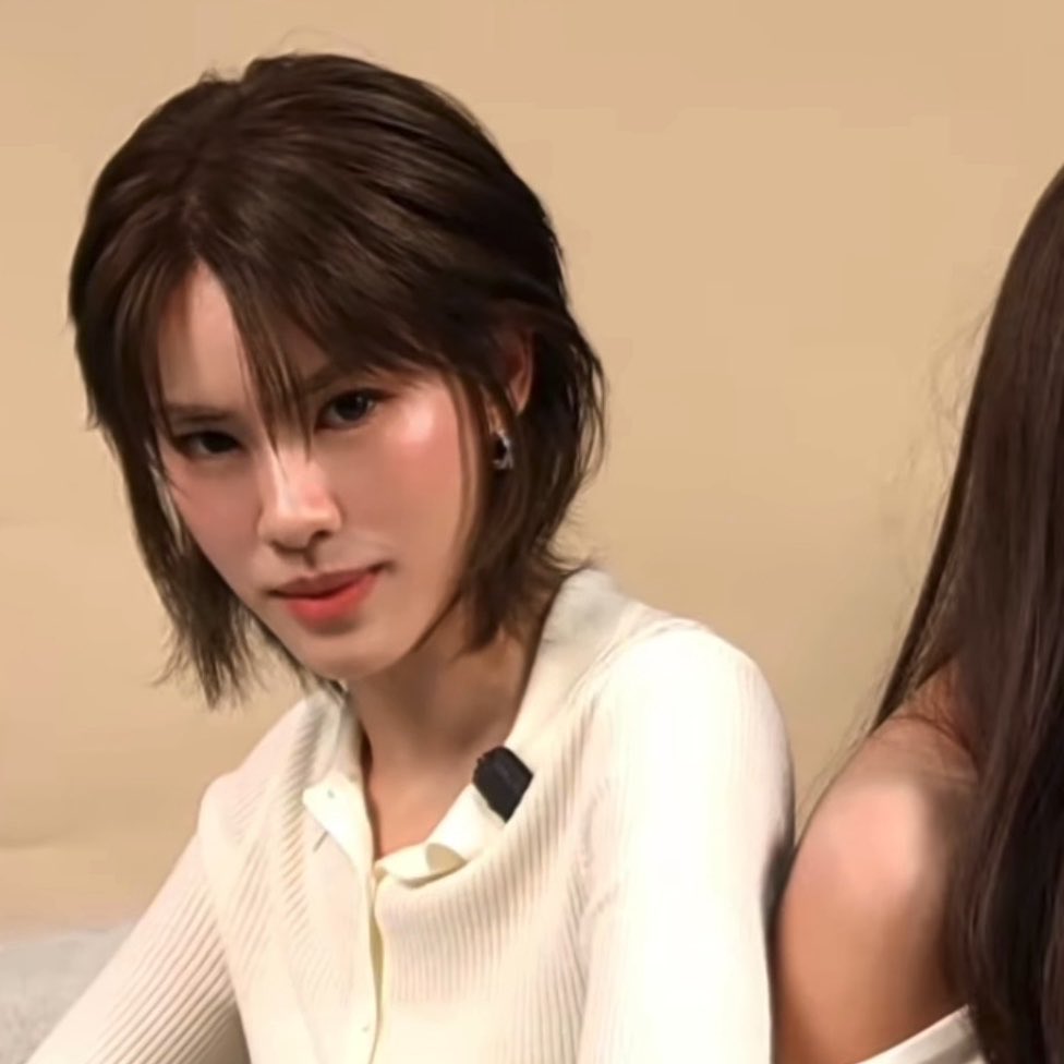 A short-haired woman in a white shirt poses for a portrait alongside another person whose shoulder is visible on the right.