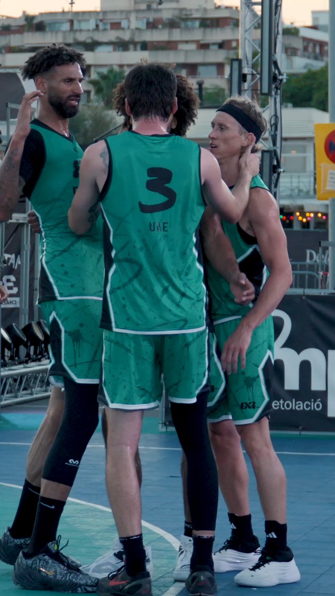 Three basketball players in green UAE jerseys, including number 3, celebrate together on an outdoor basketball court.