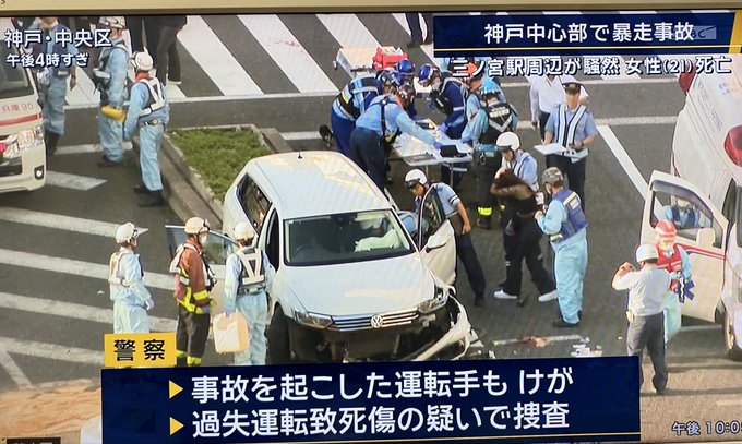 A Japanese news broadcast captures the aftermath of a violent hit-and-run accident in Kobe's Chuo Ward, showing emergency responders and police surrounding a silver Volkswagen sedan with significant front-end damage. The on-screen text announces that a female pedestrian (aged 21) died in the chaos around Sannomiya Station, while the driver is in custody on suspicion of fatal reckless driving, notably omitting the driver's identity and nationality from the coverage.
