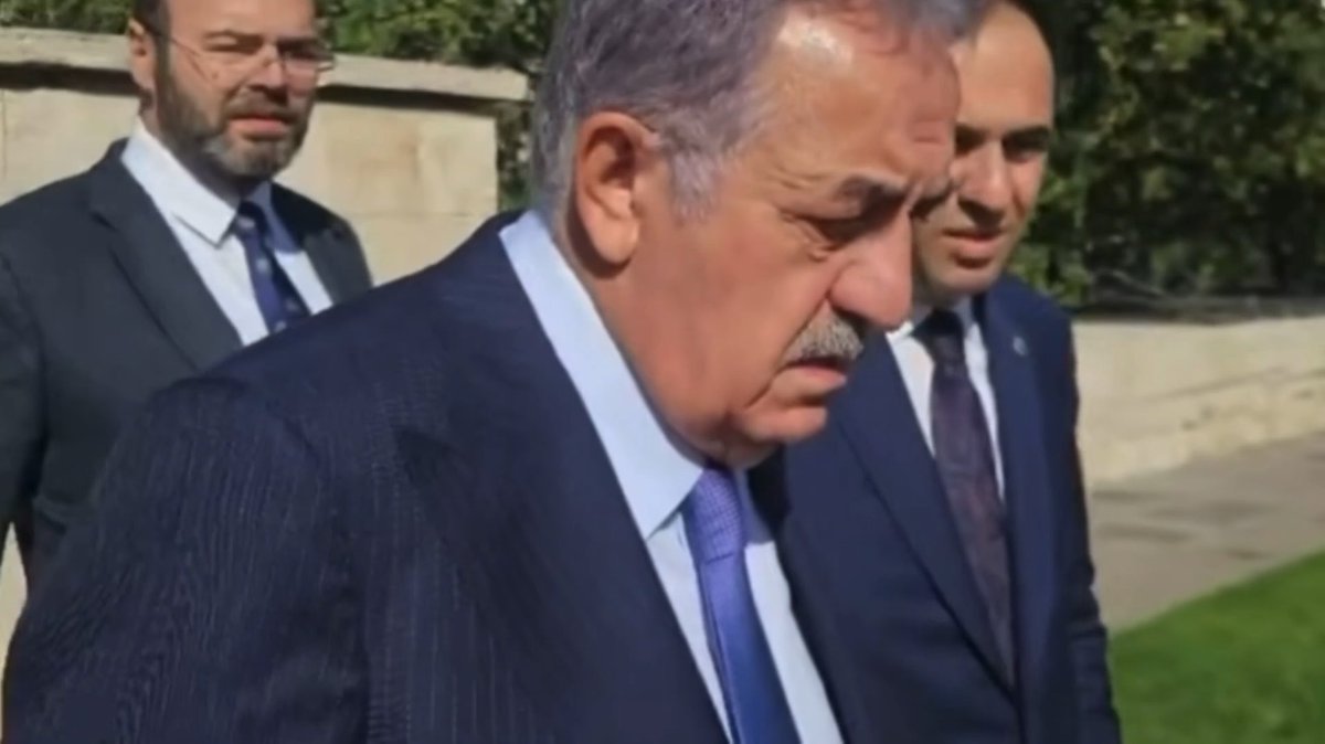 A close-up shot of Turkish President Recep Tayyip Erdoğan walking outdoors in a dark suit and blue tie, flanked by two other men in suits.