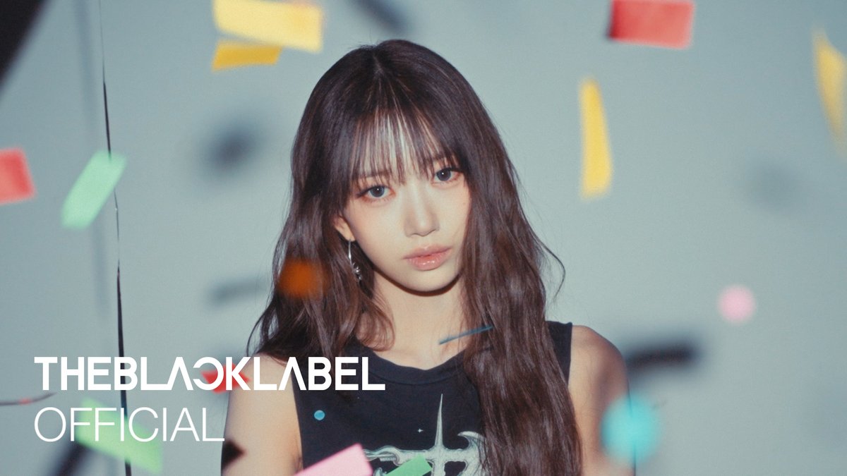 A promotional photo from 'THEBLACKLABEL OFFICIAL' featuring a young woman with long dark hair and bangs wearing a black top, posing against a background with colorful geometric shapes.