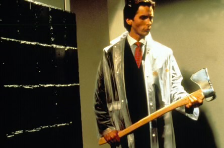 A man in a suit and clear raincoat holds a large axe in front of what appears to be stacks of black material, resembling a scene from the film American Psycho.