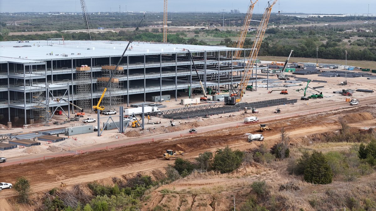 JoeTegtmeyer's tweet photo. Giga Texas Optimus factory construction update with 2 short video clips, one 360 at medium-altitude & a closer, lower flight showing tight views of the main steel structure!

Ground work started in late March, with 1st steel on May 27. By 1 October,  the frame was nearly at the north grade beam, large sections of upper floors were poured, & roofing insulation is arriving. The E side & the entire S half of the foundation have footings & grade beams, but no steel yet. The basic steel structure is ~ 40% assembled so far.

This is the dedicated high-volume 7+ million sq ft (~ 650,000 sq m) Gen 4 Optimus plant. @Tesla has not given a standalone cost, but 2026 company capex was guided at ~ $20–25 billion for AI, robotics, & factory expansion; outside estimates put the broader N Campus at ~ $5–10 billion.

This is in addition to the Fremont California Optimus plant (which is the Gen 3 pilot line) is sized at ~ 1 million units a year, expected to begin production in late 2026.

The Giga Texas plant is 10X larger & has a planned capacity of ~10 million robots a year at full scale (a long-term ceiling, not the startup rate). The current target for limited initial production is late 2027.

What is still ahead for construction over the next 6 to 8 months? Electrical conduit, water & sewage pipes, fire-water loop, storm water management drainage & underground pipes, exterior walls, roofing, ground slab & upper floor concrete & mechanical rough-in then equipment deliveries & installation. As you can see, lots of progress already, but there is a lot left to do before production line setup can happen.