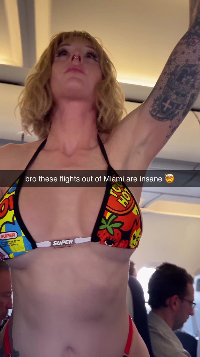 A blonde woman wearing a colorful comic-book style "SUPER" bikini stands in an airplane aisle with her arm raised to the overhead compartment, while the overlaid text reads "bro these flights out of Miami are insane 🤯"—visually illustrating the post's joke about whether you'd request a seat change next to such a striking passenger.