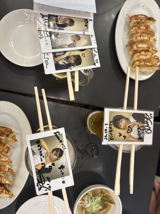 An overhead view of a table with plates of gyoza and chopsticks that have signed Polaroid photos attached to them, along with drinks.