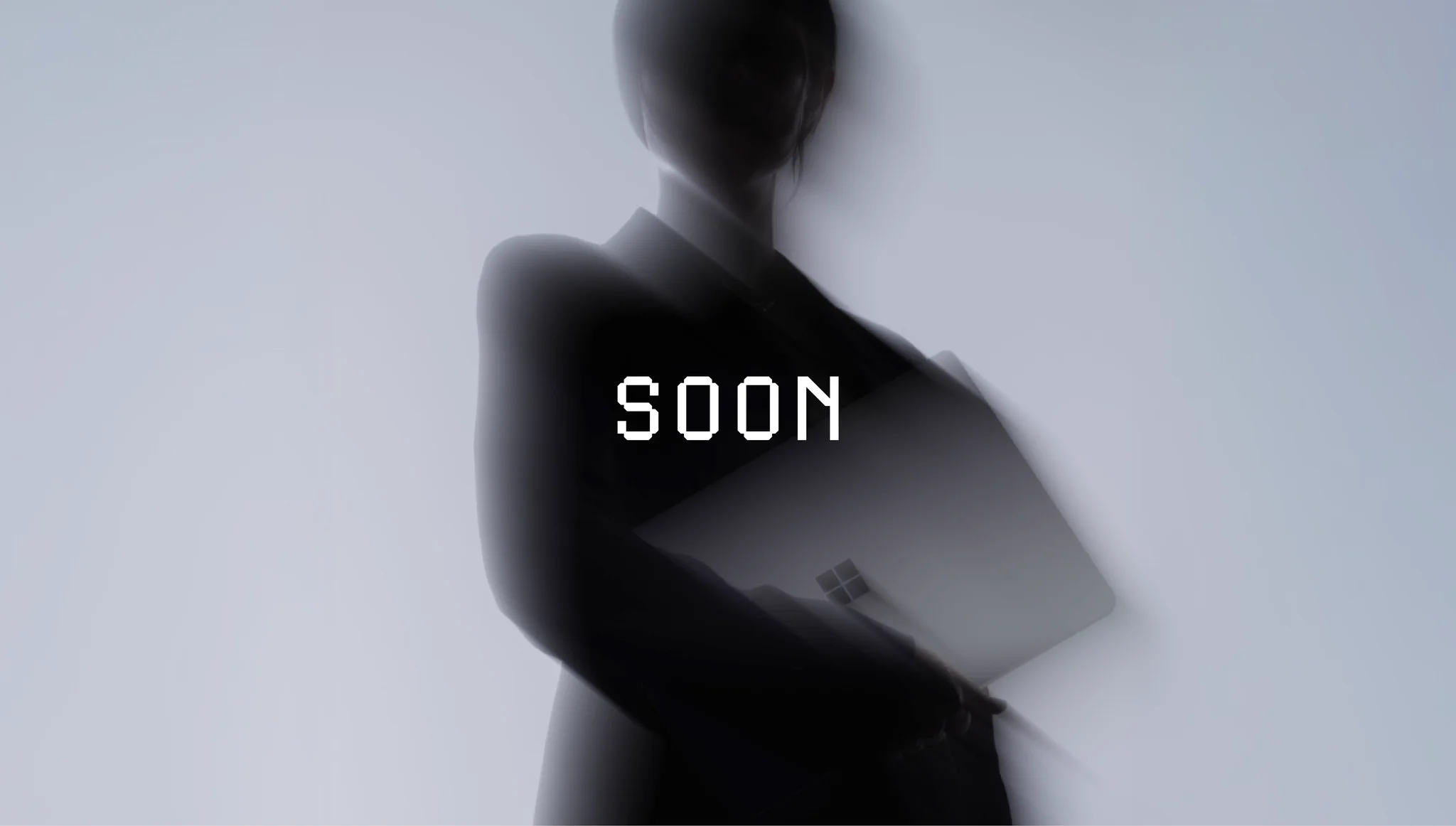 A blurred, shadowy figure in a dark blazer stands against a pale gray backdrop, holding the Surface Laptop Ultra against their side. White pixel-style text in the center reads "SOON." 
