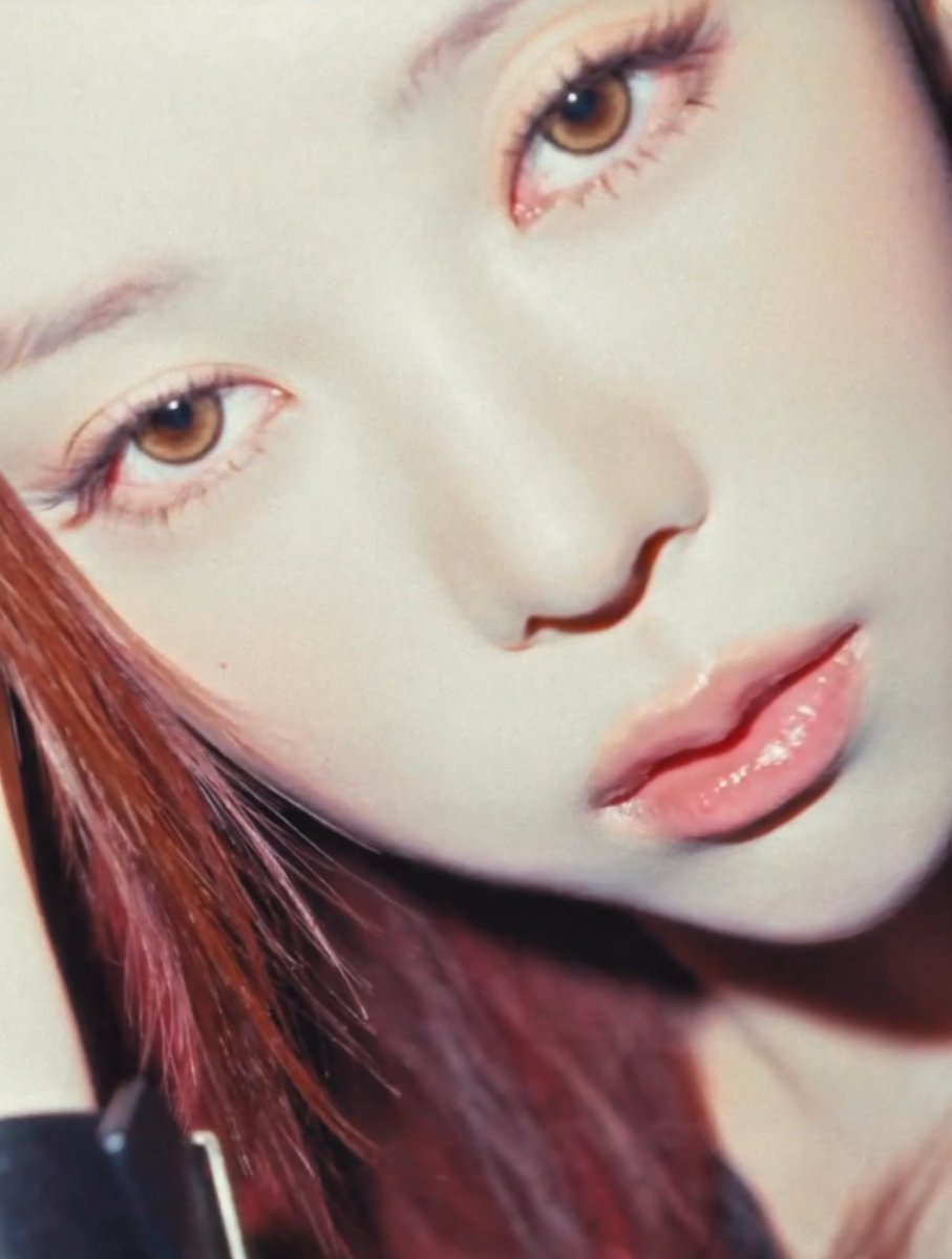 Close-up portrait of a woman with reddish-brown hair, brown eyes, and glossy pink lips, looking upward.