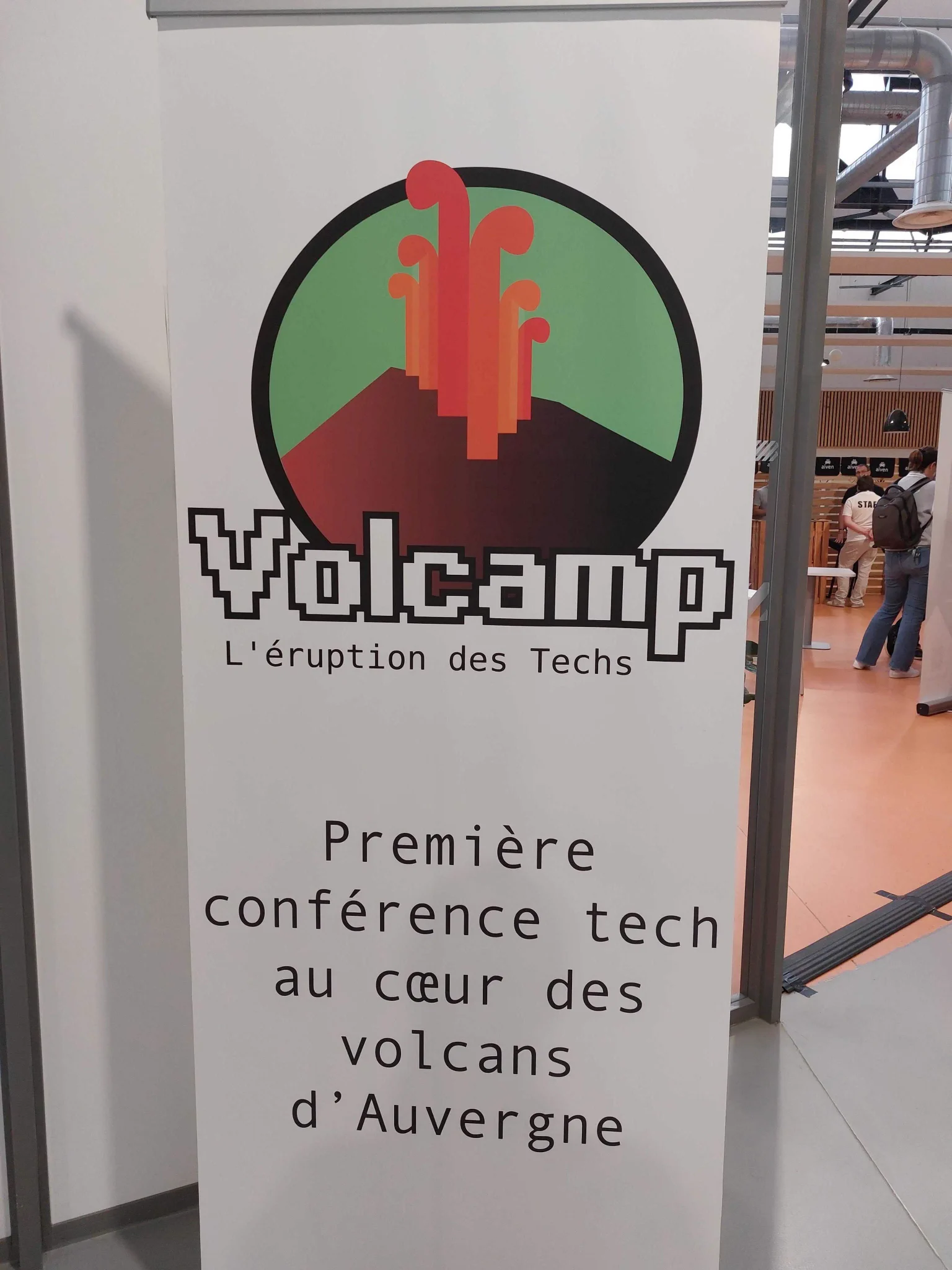 Kakémono de Volcamp affichant le logo formé d'un volcan pixelisé et les textes "L'éruption des Techs" et "Première conférence tech au coeur des volcans d'Auvergne"