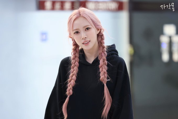 A photograph captures a young woman with long pink hair styled in twin braids, wearing a black hoodie, with Korean text '가나콜' visible in the upper right corner.