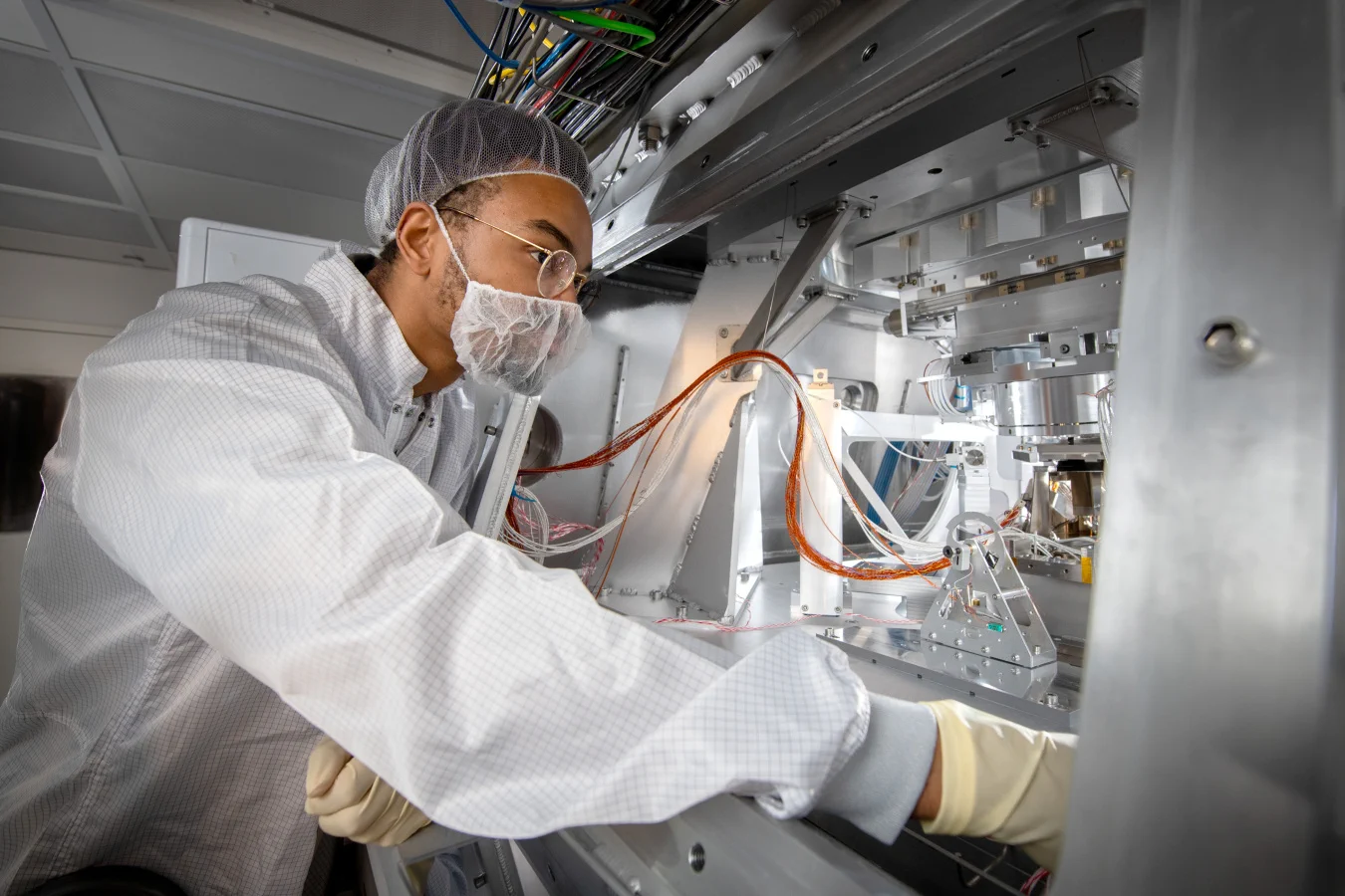 Alex Orimoloye (a man in a clean room suit) inspects part of the CXRO beamline, which is within a vacuum chamber.