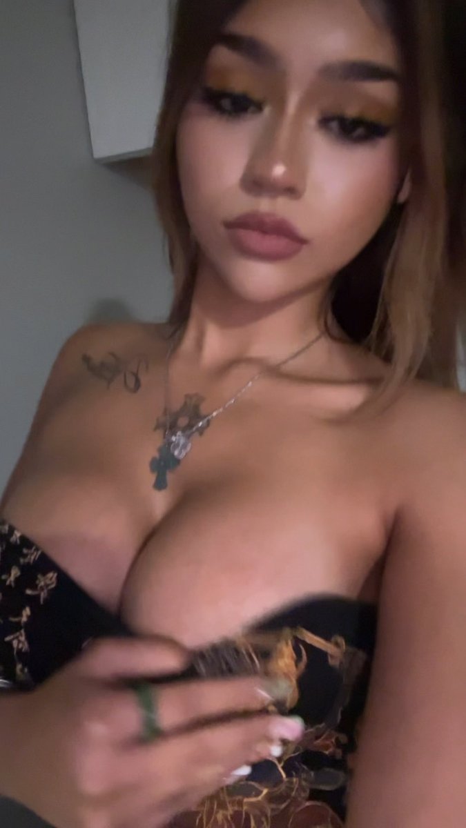 The image shows a young woman taking a mirror selfie while wearing a strapless black and gold patterned top, with visible neck tattoos and a pendant necklace, posing in what appears to be a bathroom. The caption "Good morning! Text me" suggests she's starting her day and inviting followers to message her, aligning with the casual, inviting tone of her selfie.