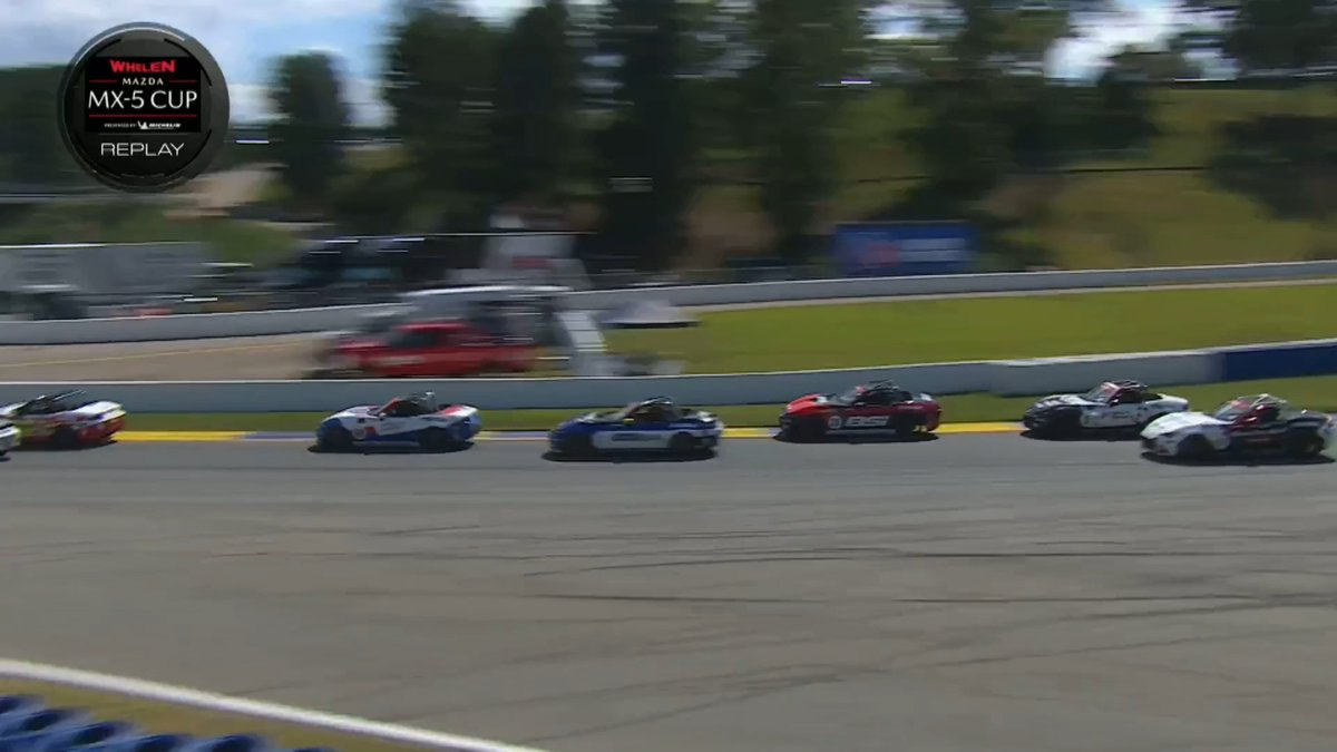 A replay video screenshot from the 'Whelen Mazda MX-5 Cup' shows several race cars in blue, red, and white driving on a circuit track.