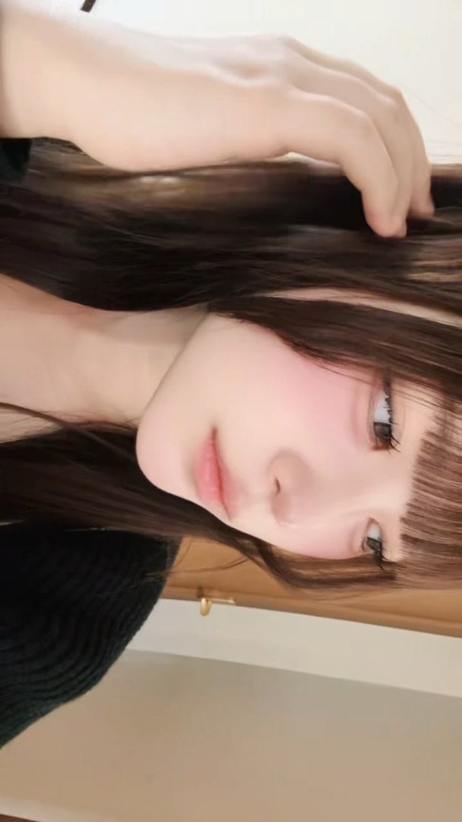 Selfie portrait of a young woman with long dark hair and bangs, shown in a rotated/sideways orientation with her hand running through her hair.