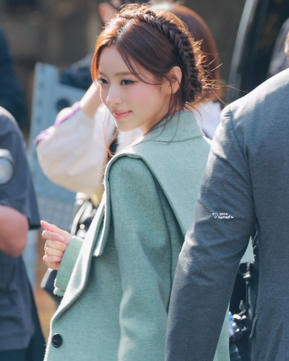 A young woman with braided hair wearing a light green coat looks over her shoulder in an outdoor setting with a watermark 'ama rated' visible.