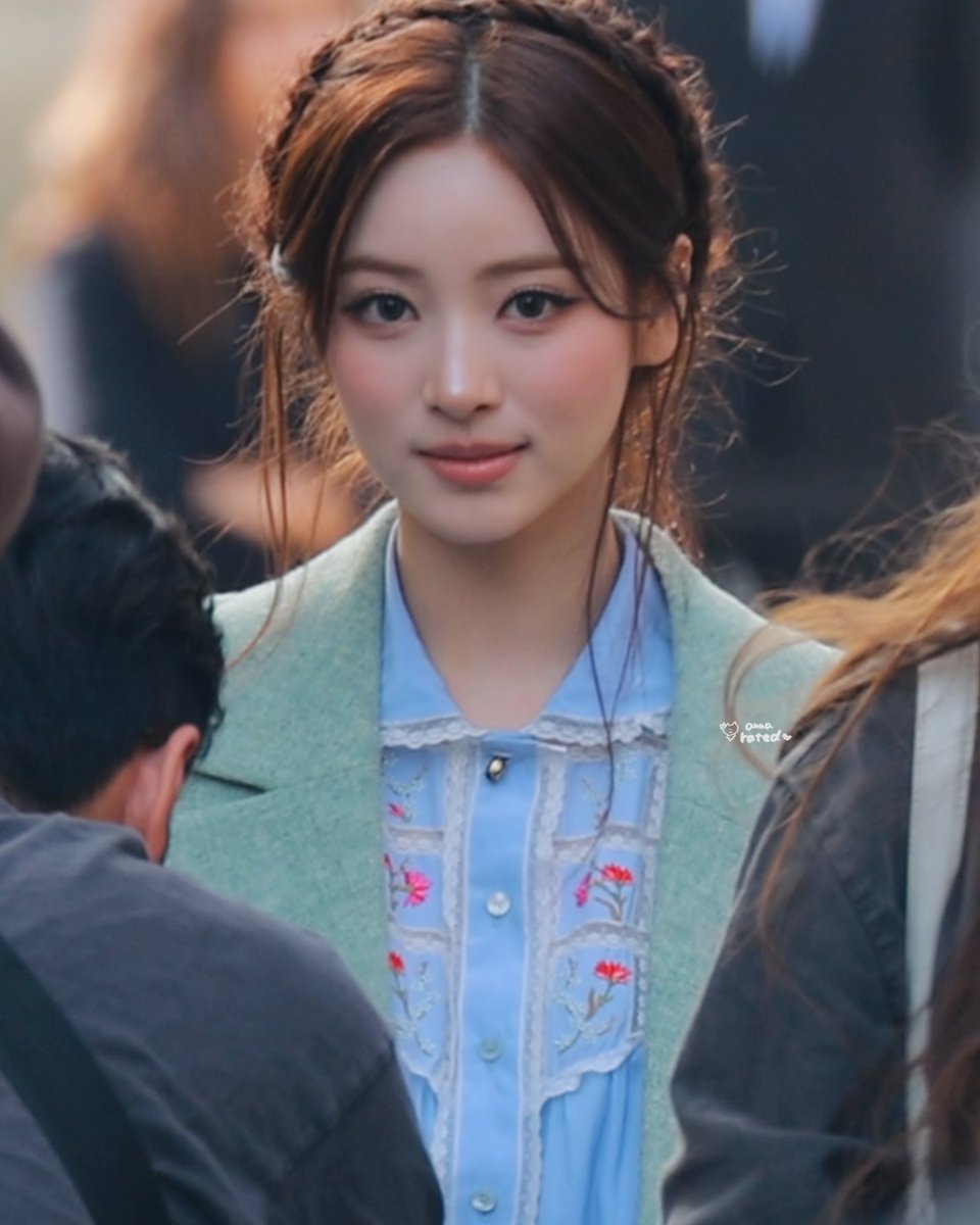 A close-up shows a young woman with braided hair wearing a light blue embroidered blouse under a mint green blazer, with a faint watermark reading 'omo rated'.