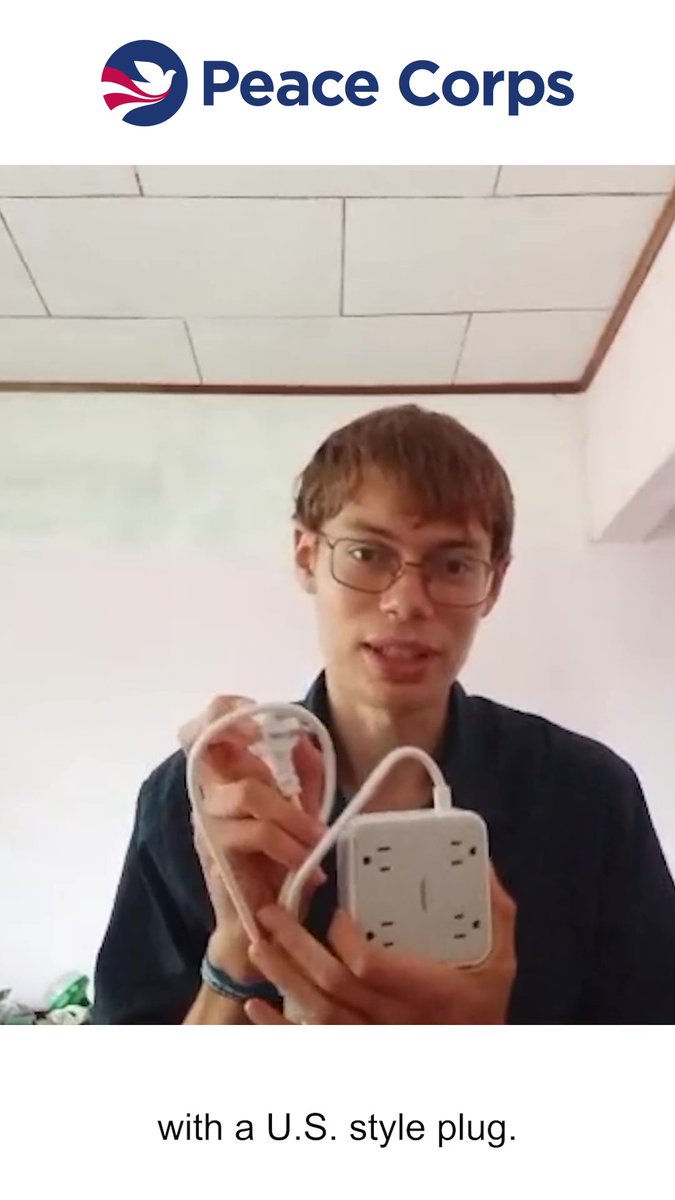 A man wearing glasses holds a power adapter with multiple outlets. The Peace Corps logo is at the top, and the caption reads 'with a U.S. style plug.'