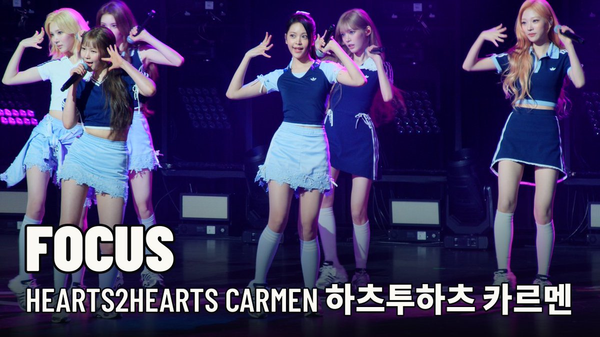 Five female performers dance on stage in matching schoolgirl-inspired outfits, with text reading 'FOCUS HEARTS2HEARTS CARMEN 하츠투하츠 카르멘'.