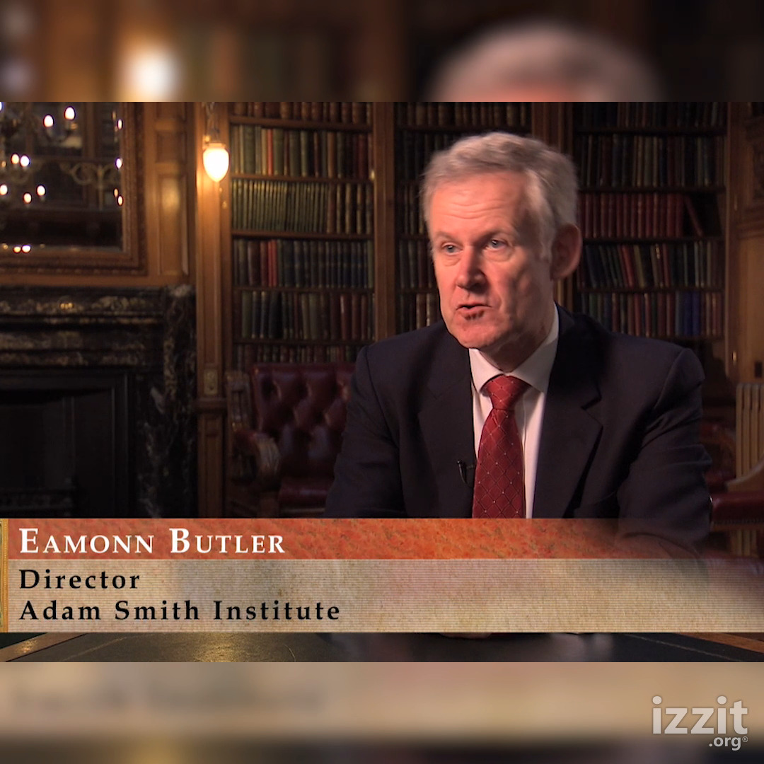 An interview shot of an older man in a suit and red tie seated in a library; on-screen text identifies him as 'Eamonn Butler, Director, Adam Smith Institute' with an 'izzit.org' logo.