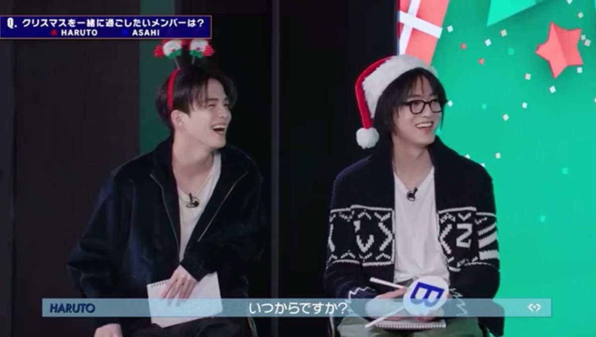 A screenshot from a video featuring two members (HARUTO and ASAHI) of a K-pop group wearing Christmas headbands, with on-screen text in Japanese including a question about which member they would want to spend Christmas with.
