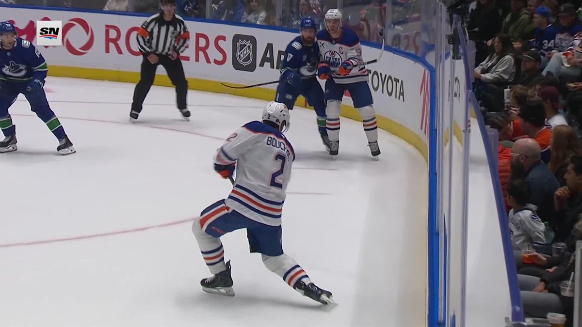 An NHL hockey game in progress shows a Vancouver Canucks player (#2 Bouchn...?) skating while Edmonton Oilers players stand against the boards, with Rogers and Toyota advertisements visible.