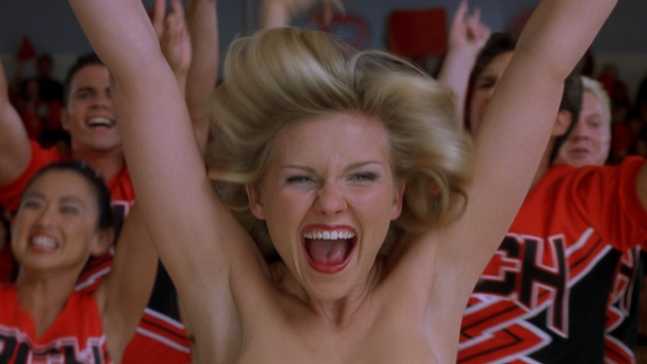 A blonde cheerleader screams with intense excitement, her arms raised triumphantly, while fellow cheerleaders in red and black uniforms cheer enthusiastically behind her. The image captures the high-energy, passionate atmosphere typical of a sports team's introduction, fitting the caption "this intro" which references an energetic opening or hype sequence.
