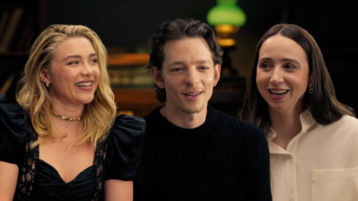 The image shows Florence Pugh, Mike Faist, and Zoe Kazan from "East of Eden" sitting together during an interview, with all three appearing engaged and amused, likely reacting to the playful comment about Mike looking hot.