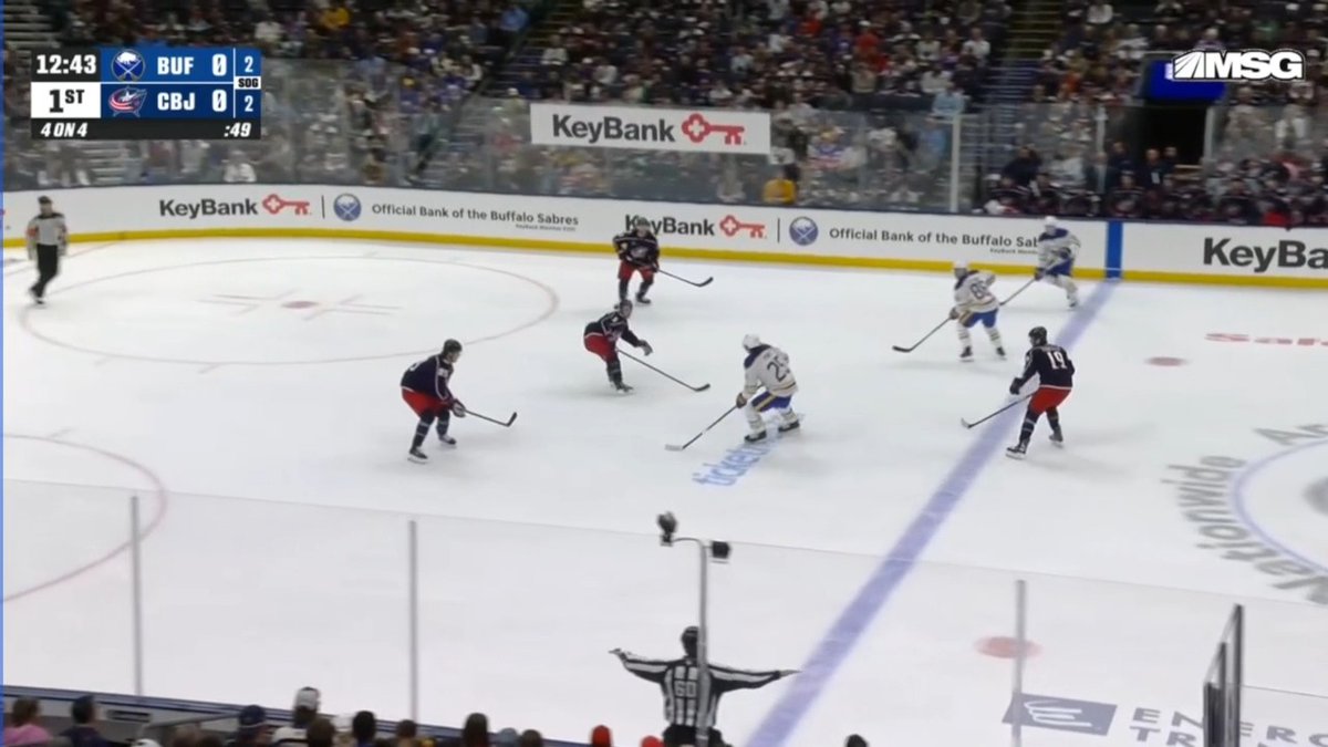 A Buffalo Sabres hockey game is underway against the Columbus Blue Jackets, with the scoreboard showing a 0-0 tie at 12:43 in the 1st period during a 4-on-4 situation. The Sabres are on the power play attacking into the offensive zone, with KeyBank advertisements visible on the boards as fans fill the stands behind the glass.