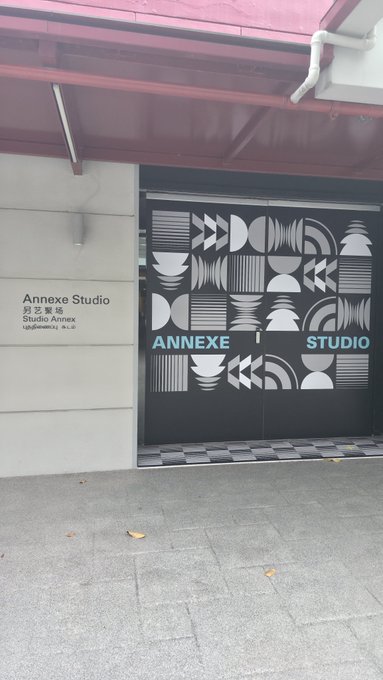 A photograph shows the entrance to a building with black double doors featuring a geometric white pattern and the text 'ANNEXE STUDIO' in blue and white, next to a wall plaque reading 'Annexe Studio' in English, Chinese, and Japanese characters.