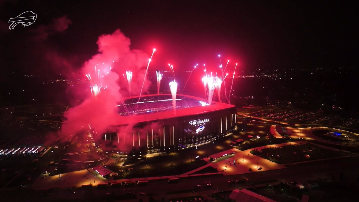 An aerial nighttime view captures Highmark Stadium illuminated by red fireworks bursting overhead, with the "HIGHMARK STADIUM" sign and Buffalo Bills logo prominently displayed on the stadium's facade, perfectly complementing the post's celebration of the team's home opener.