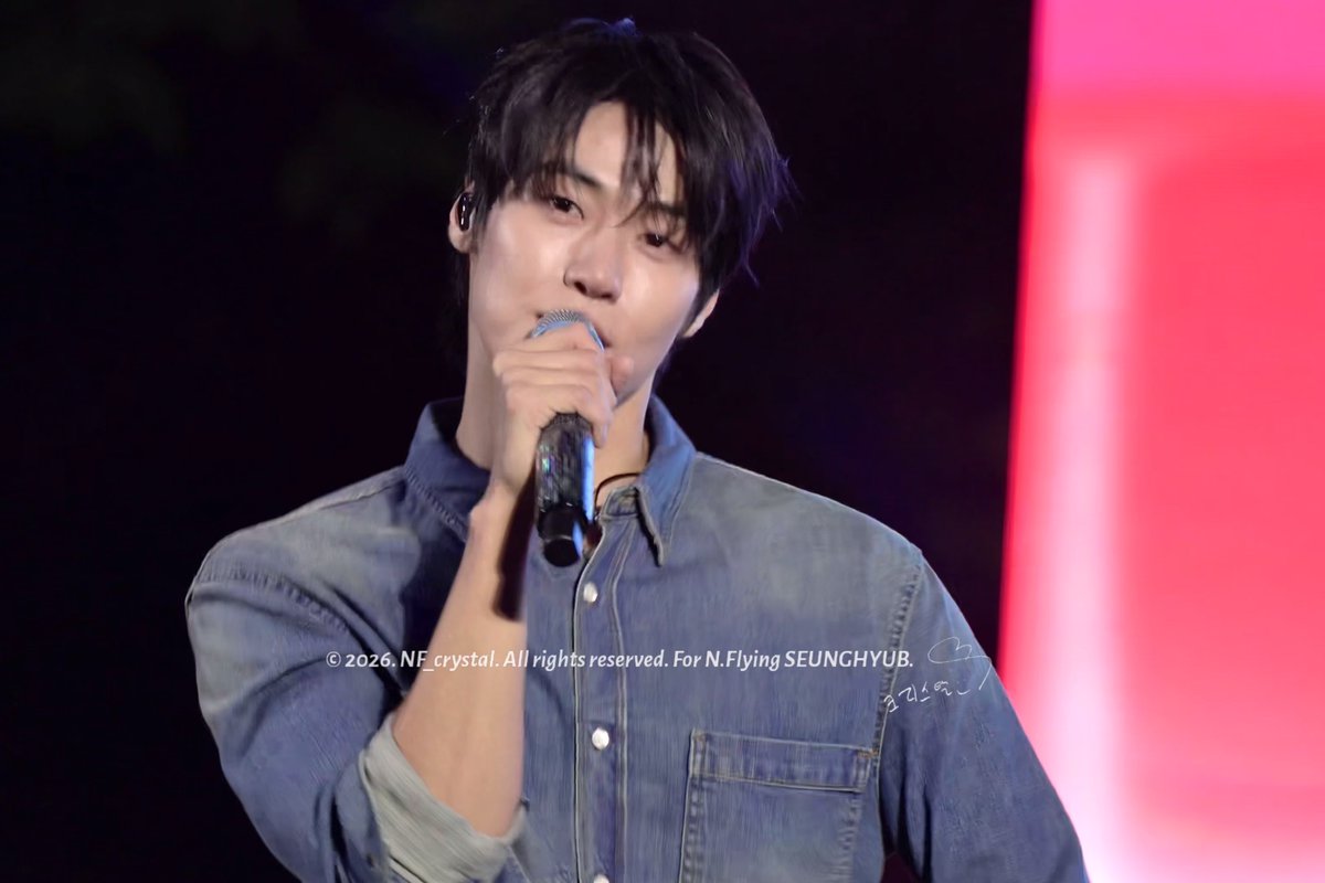A young male performer in a denim shirt singing into a microphone on stage with red lighting, watermarked '© 2026. NF_crystal. All rights reserved. For N.Flying SEUNGHYUB.'