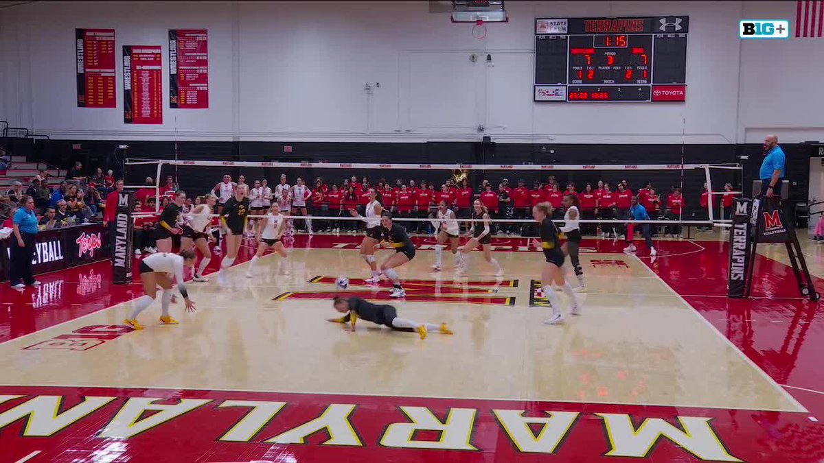 A women's college volleyball match between Maryland and an opposing team in black, with a scoreboard showing Maryland leading 87-87 in the 4th period.