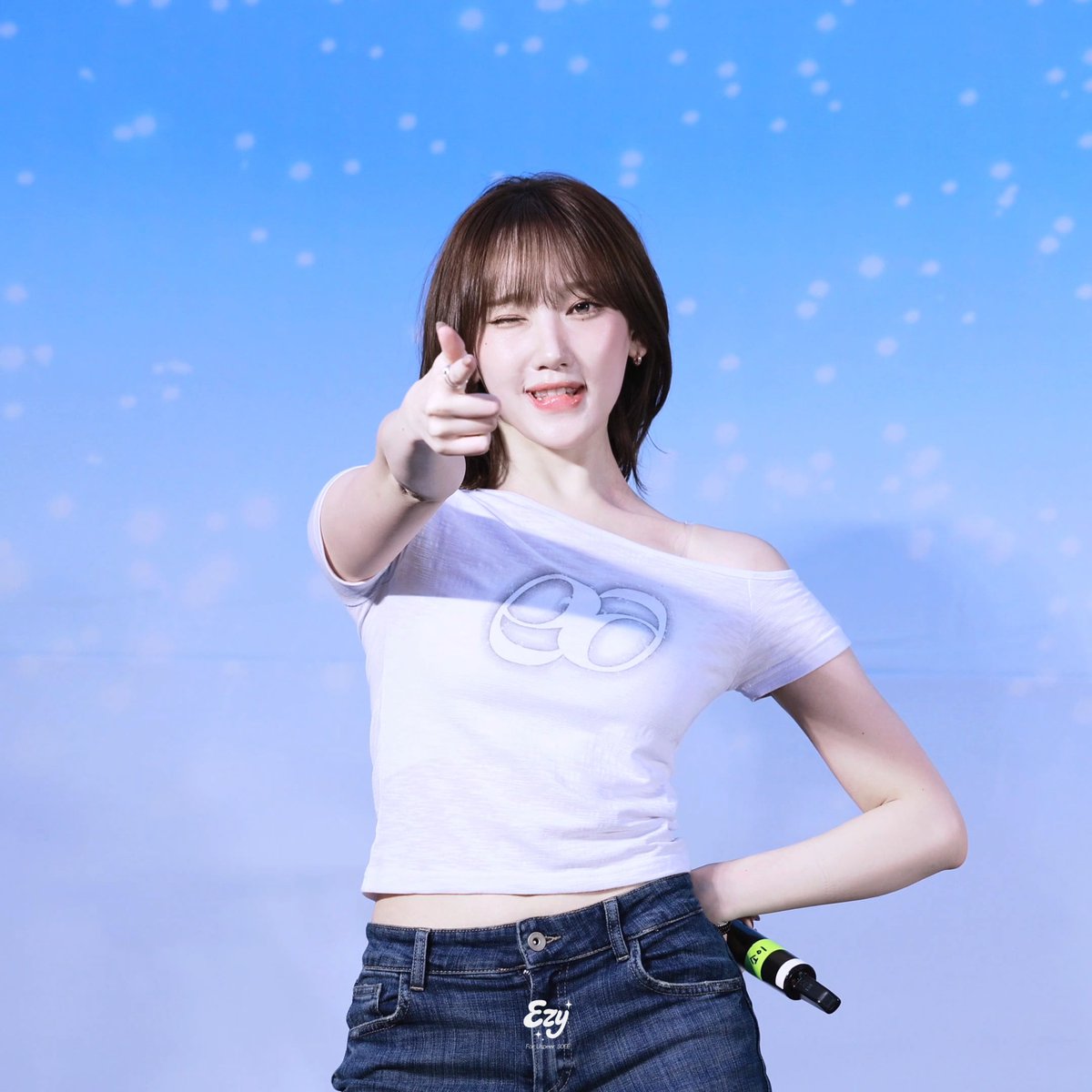 A smiling woman with short hair winking and pointing at the camera while wearing a white off-shoulder shirt with an infinity logo, with a watermark reading 'Ezy For Ulike Q3EE'.