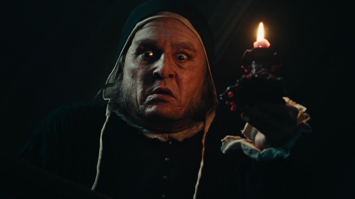 Johnny Depp appears as a wide-eyed, disheveled Ebenezer Scrooge clutching a single flickering candle in a dimly lit scene from the film *Ebenezer*, arriving in theaters November 13.