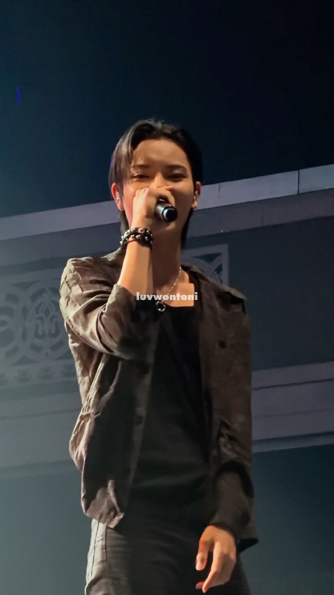 A male performer on stage sings into a microphone, wearing a dark jacket and necklace, with the watermark "luvwontoni" visible.