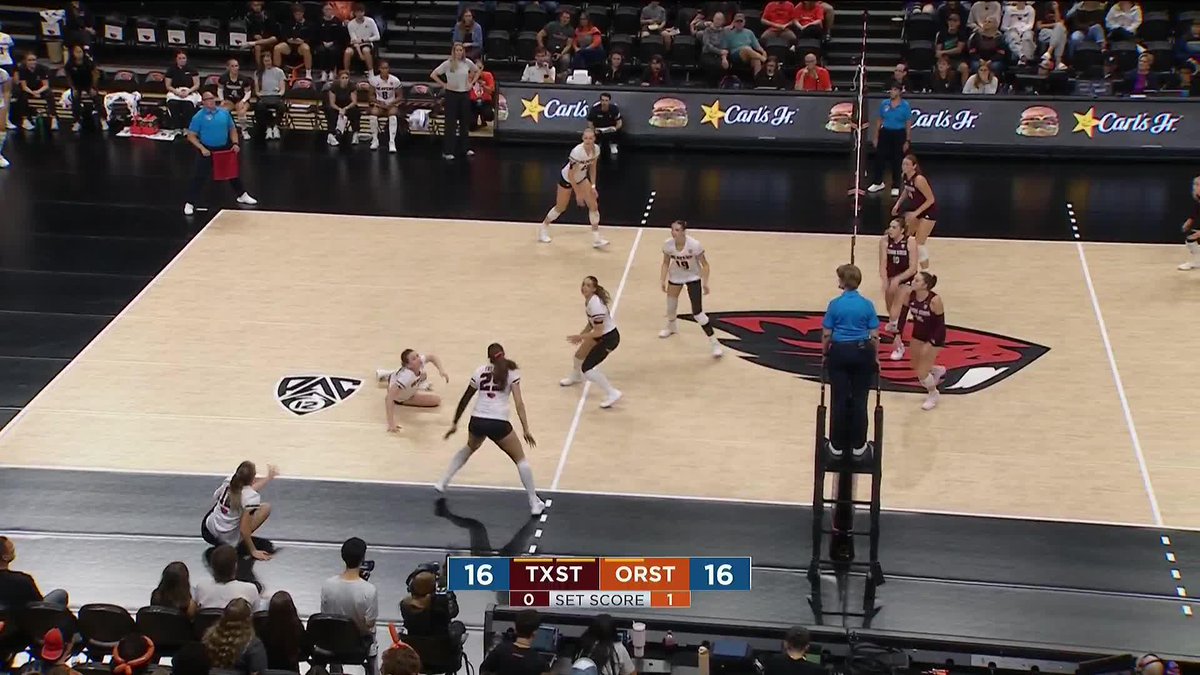 An indoor volleyball match in progress between teams in white (TXST) and maroon (ORST), with the score tied at 16 and the first set score showing 0-1, on a court with an Oregon State logo.