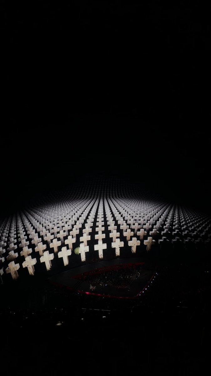 A darkened arena illuminated by hundreds of white cross-shaped lights arranged in rows converging toward a central stage, evoking a solemn, cathedral-like atmosphere fitting for the heavy metal performance by Metallica that the post references.