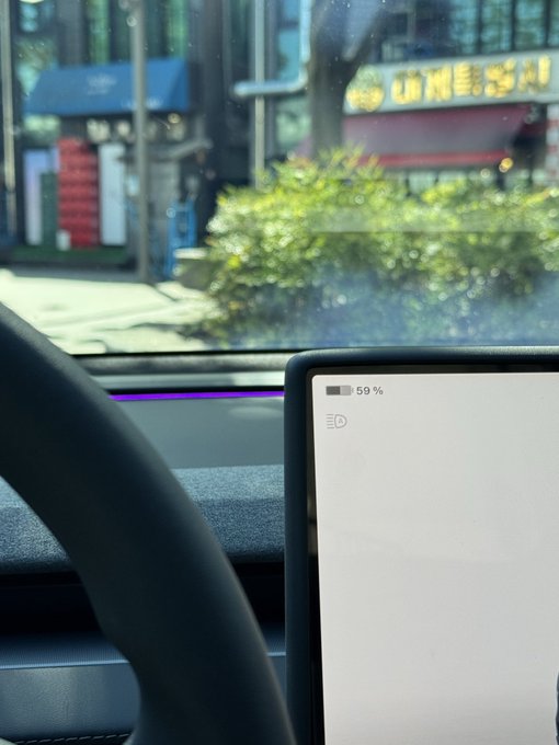 The dashboard of a car, showing the steering wheel and center screen at 59% battery, with blurred storefronts visible through the windshield.