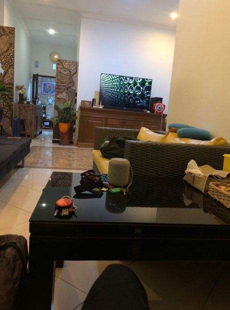 A living room interior showing a flat-screen TV displaying a green patterned design, a yellow couch with cushions, a black glass coffee table, and wicker furniture.