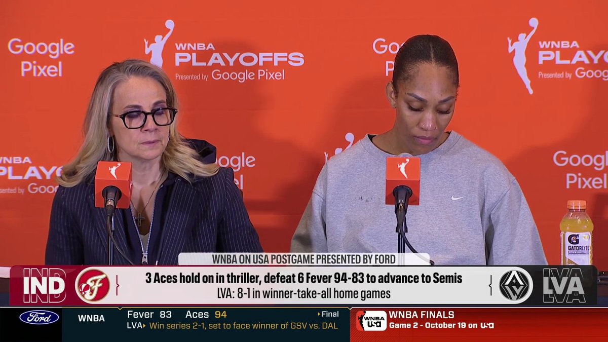 Two women sit at a press conference table in front of a WNBA Playoffs backdrop with microphones, the on-screen graphics showing the Las Vegas Aces defeating the Indiana Fever 94-83 to advance to the Semifinals, contextualizing A'ja Wilson's comments about not letting emotions from the Game 2 incident distract her team during Game 3.