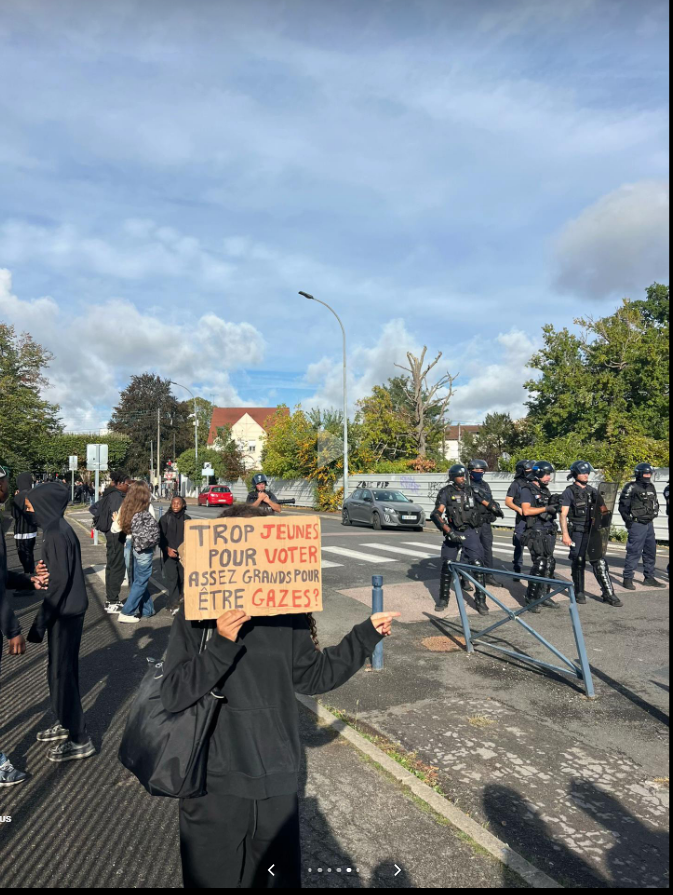 SeraphineMoreau's tweet photo. Une manifestante avec une pancarte portant l'inscription 
« TROP JEUNES POUR VOTER,
ASSEZ GRANDS POUR ÊTRE GAZÉS ! »
face aux forces de l'ordre, dans le cadre du mouvement de contestation et des blocus lycéens en France, fin septembre et début octobre 2026. https://t.co/dTvygoOO2p