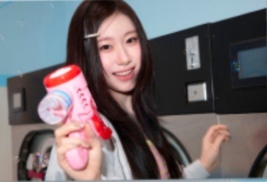 A young woman with long dark hair smiling and holding a pink and white bubble gun toy, standing in front of laundry machines.