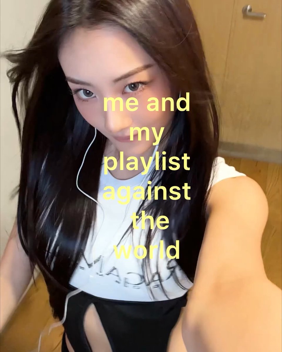 A selfie of a young woman with long dark hair wearing earphones and a white t-shirt, with yellow text overlay reading 'me and my playlist against the world'.